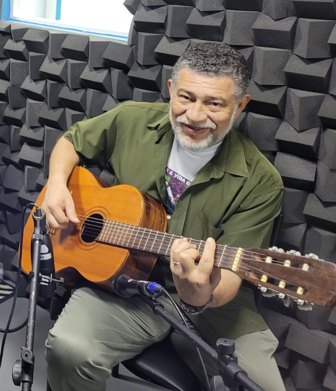 Clóvis Ribeiro sorrindo e segurando um violão no estúdio de gravação